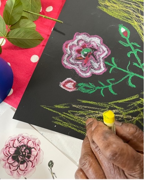 Hand drawing a pink rose in oil pastel on black paper during a workshop at The Islington Centre