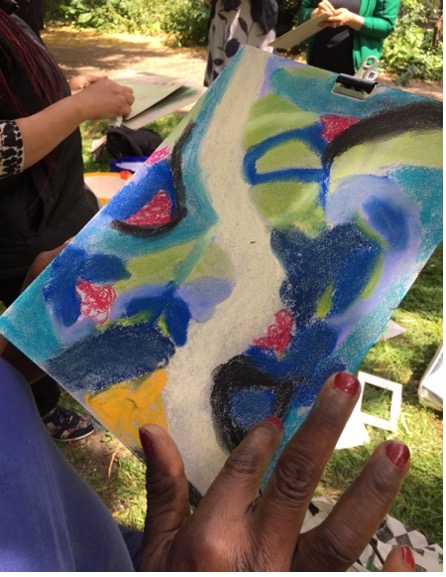 A vibrant blue and green oil pastel painting held up outdoors during a teaching session